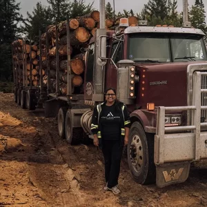Rajni from Ayat Timbers International standing in front of a log truck at their sawmill in New Brunswick, Canada, specializing in wood siding, custom milling, and tongue and groove pine production.